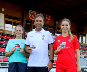 Zwei Fußballspielerinnen und der Trainer halten eine Dauerkarte in der Hand