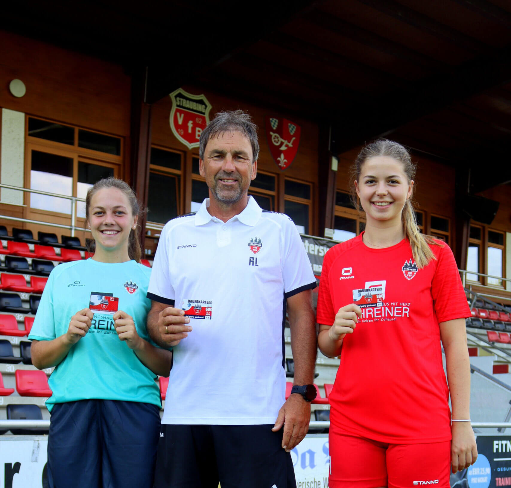 Zwei Fußballspielerinnen und der Trainer halten eine Dauerkarte in der Hand